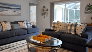 A living room with two dark grey sofas, a glass coffee table, and a large window with a view of the outdoors.
