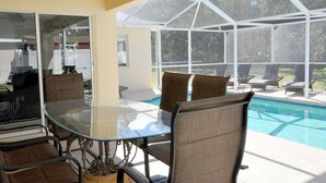 A sunroom with a glass table and chairs, a pool, and a view of the outdoors.