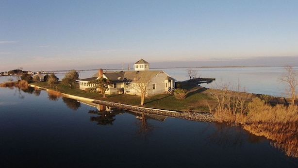 Uma casa com um gramado amplo e um píer que se estende por um lago calmo.