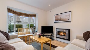 Ein modernes Wohnzimmer mit Kamin, Flachbildfernseher und großem Fenster mit Jalousien.