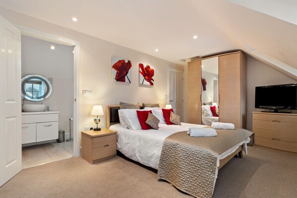 A modern bedroom with a large bed, a TV, and a walk-in closet.