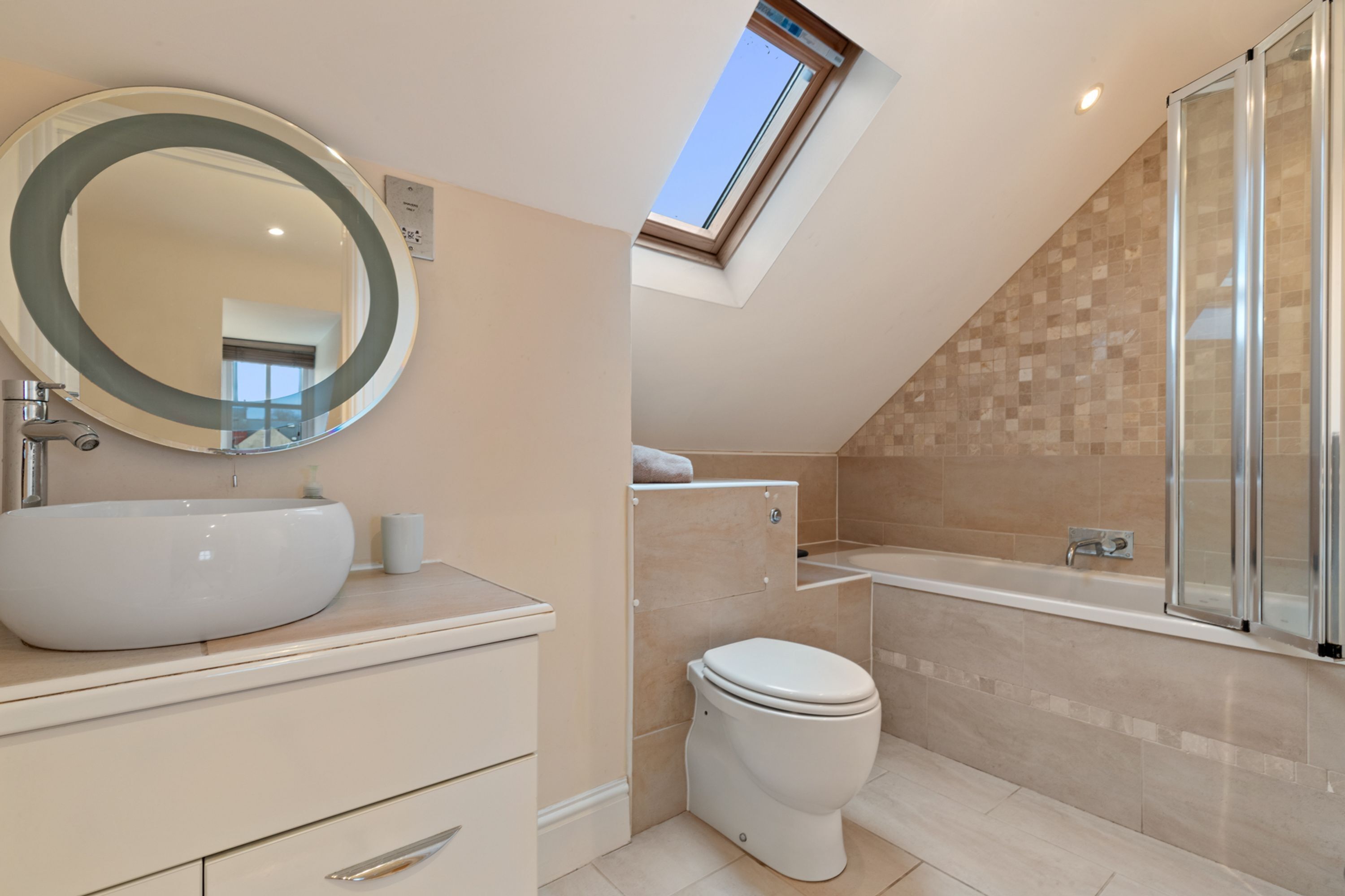 A modern bathroom with a skylight, a large oval sink, a toilet, and a glass-enclosed shower area.