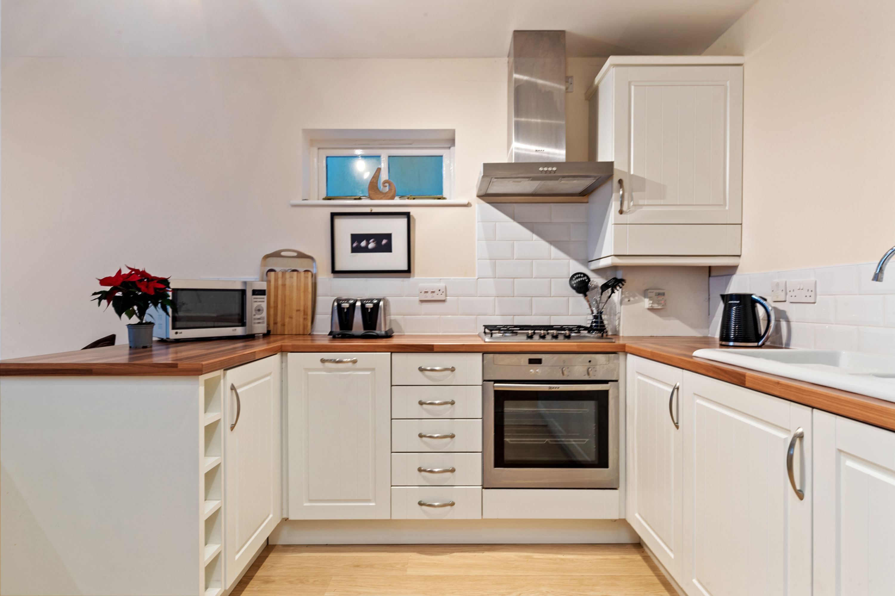 A modern kitchen with white cabinets, a microwave, a toaster, a stove, and a sink.