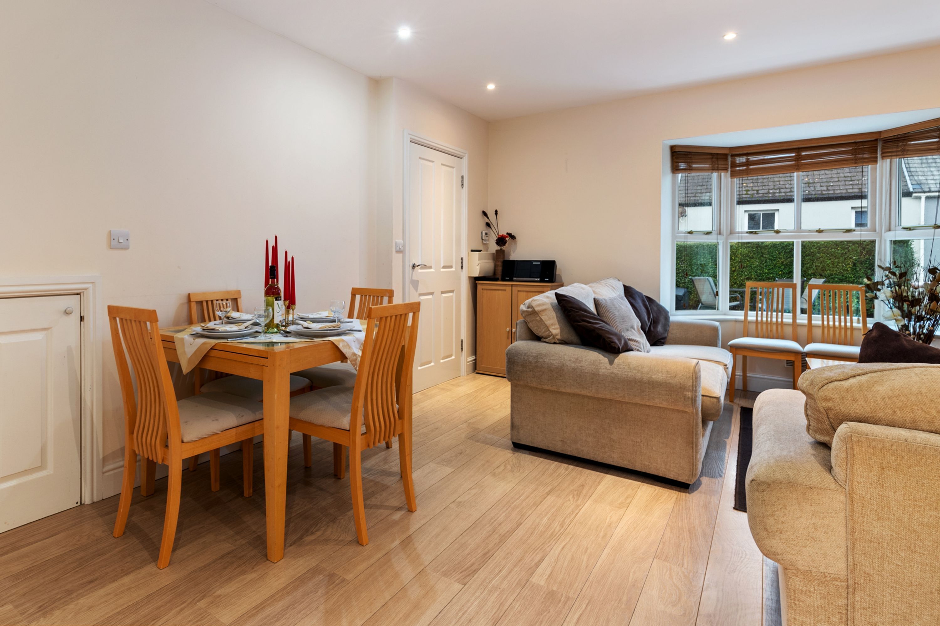 A modern living room with a dining area, wooden furniture, and large windows.