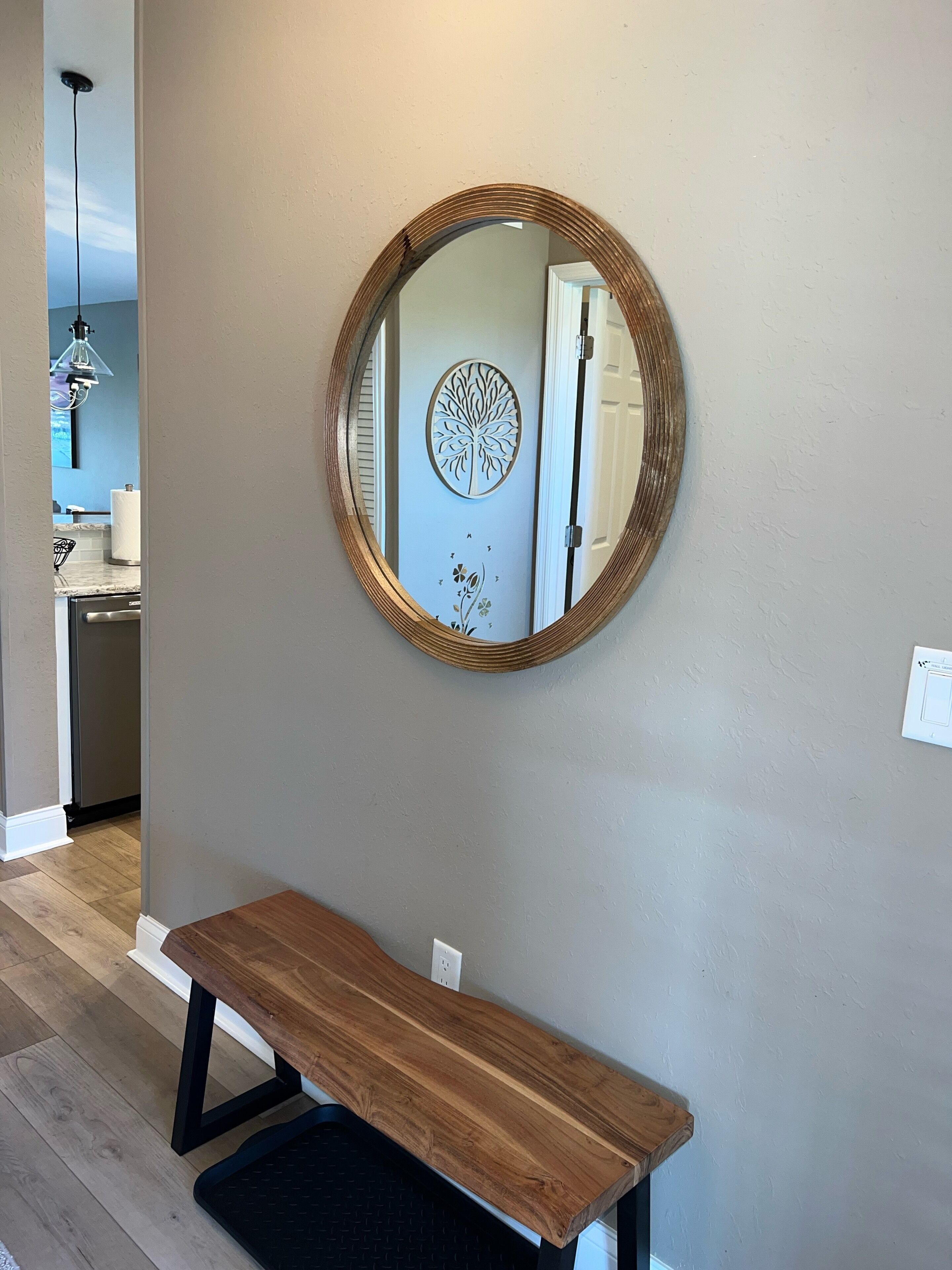 Un pasillo con un espejo redondo en la pared, un banco de madera y una puerta con panel decorativo.