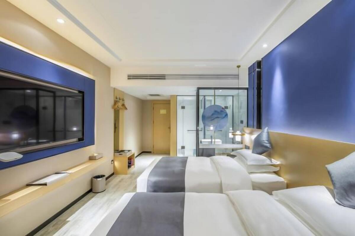 Una habitación de hotel moderna con una cama grande, un televisor montado en la pared y un mamparo de vidrio que da al baño.