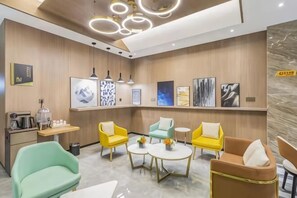 A modern hotel lobby with a reception desk, seating area with yellow and green chairs, artwork on the walls, and pendant lighting. - XIANG GE LI TING HOTEL (Xiuwu)