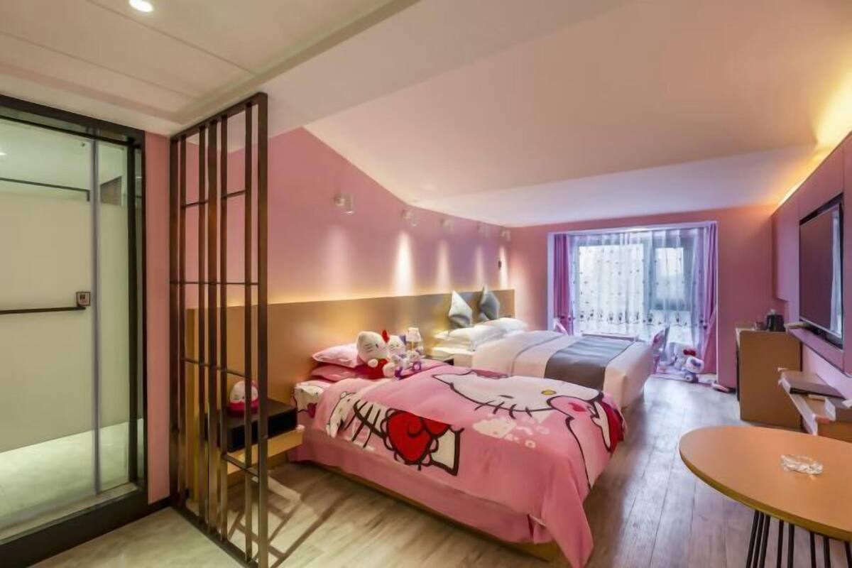 Habitación de hotel en tonos rosados, con una cama, un escritorio y un ventanal.