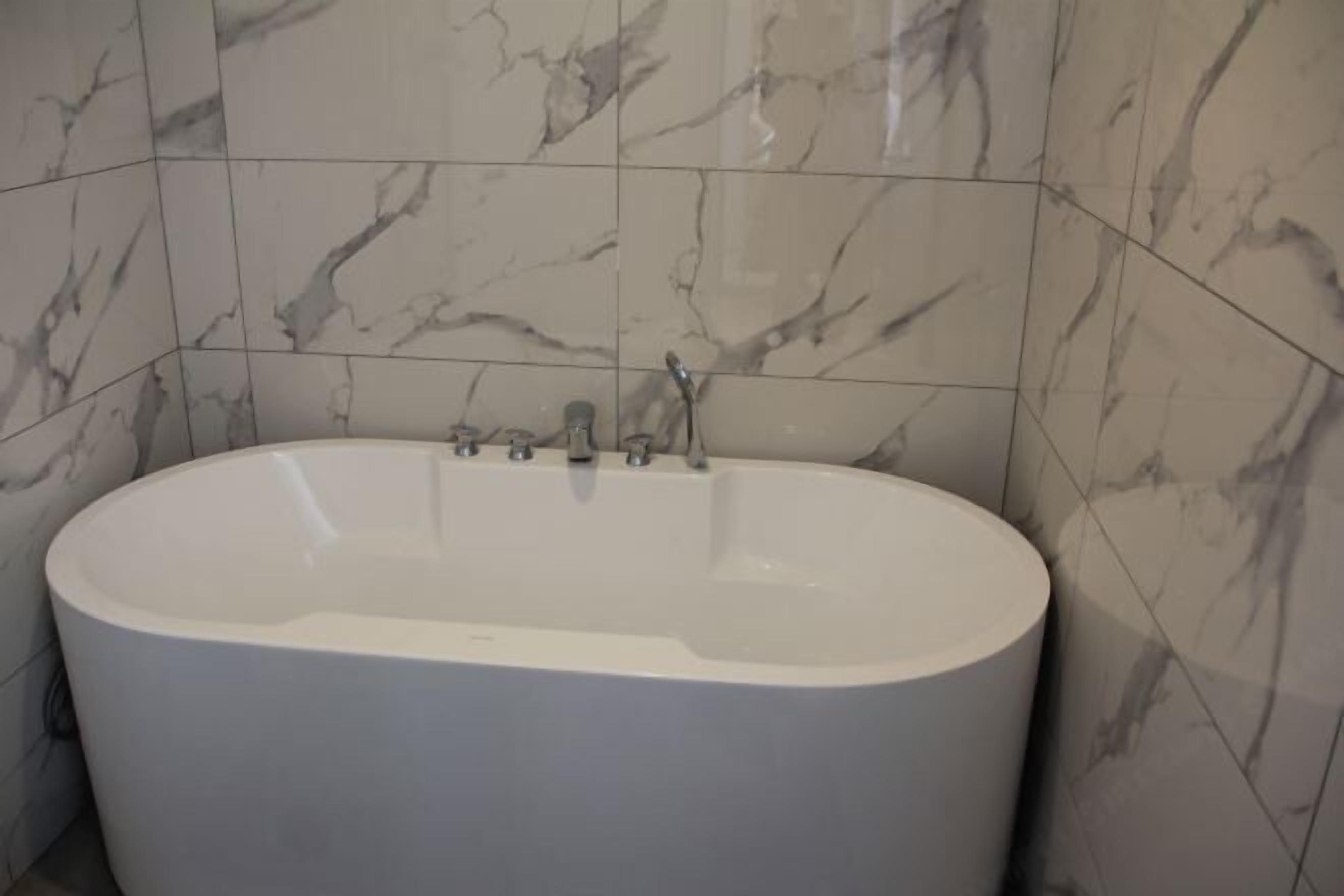 A modern bathroom with a freestanding bathtub, marble tiles, and a visible showerhead.