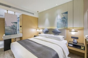 A modern hotel room with a large bed, bedside tables, a mirror, and abstract wall art.