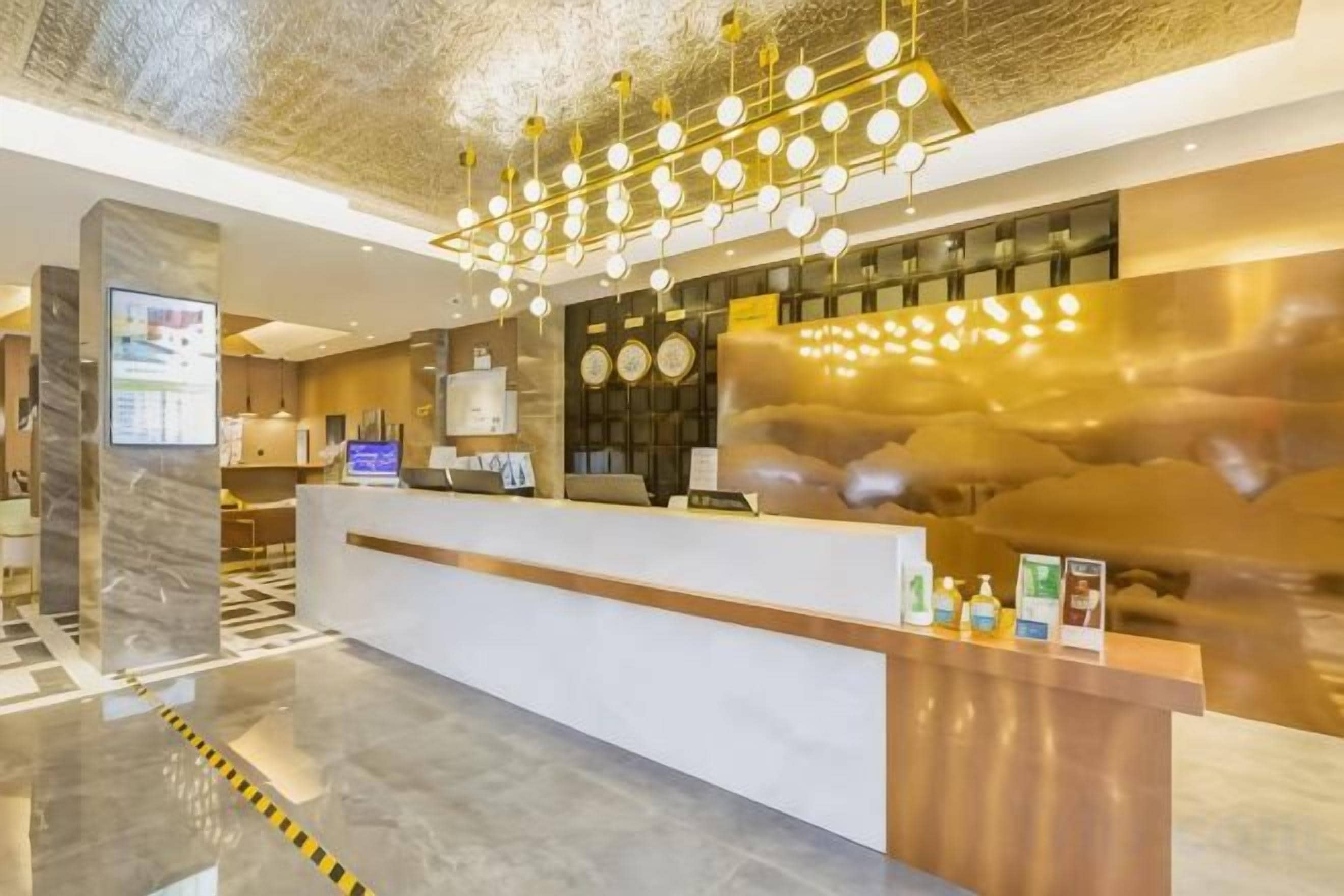 A hotel reception area with a marble floor, a reception desk, a digital screen, and a modern chandelier.