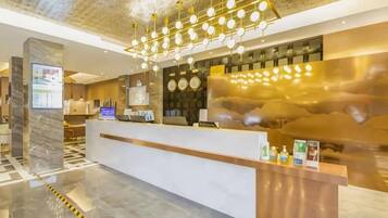 A hotel reception area with a marble floor, a reception desk, a digital screen, and a modern chandelier.