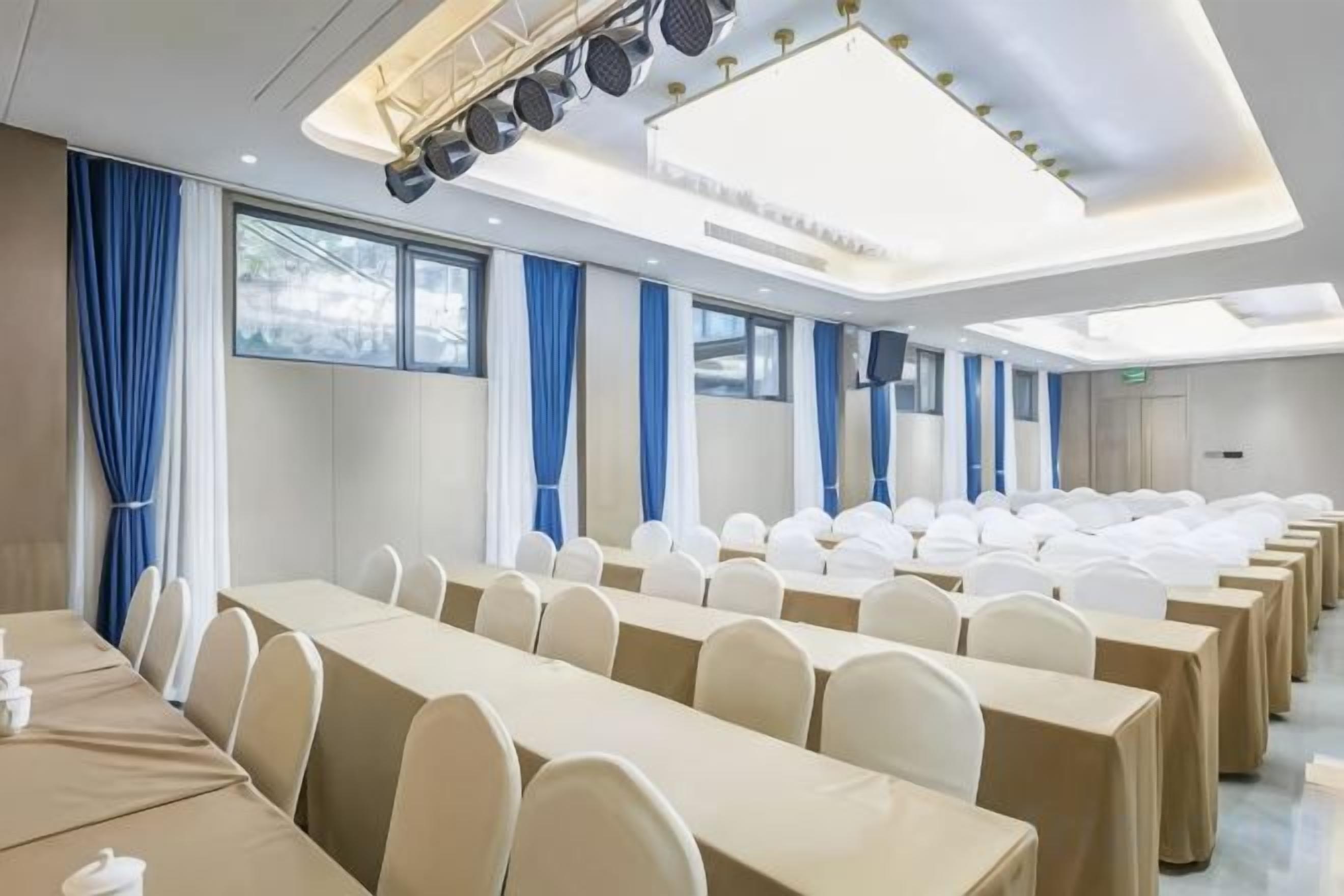 Un salón de conferencias con filas de mesas y sillas, ventanas amplias y un diseño moderno del techo.