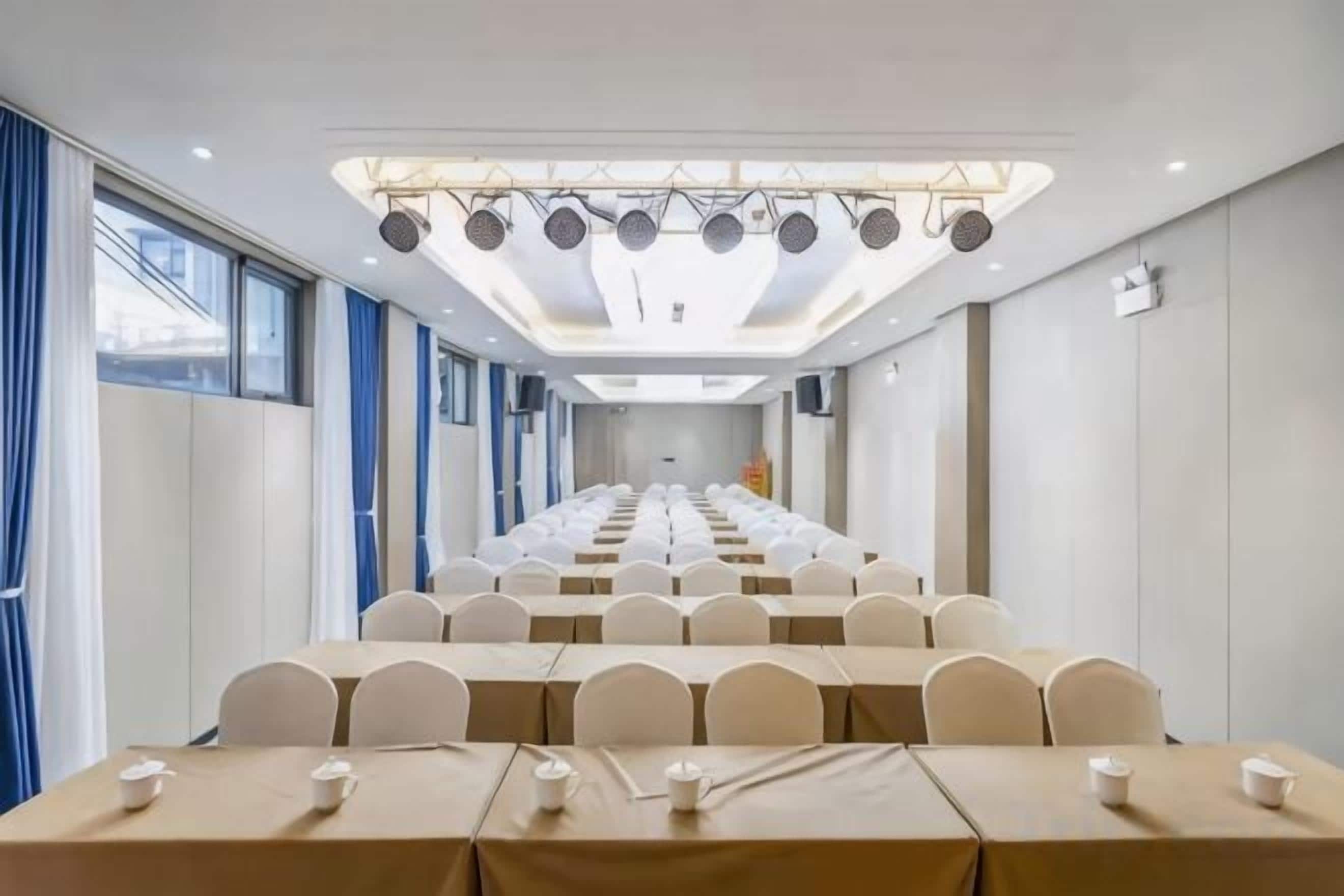 A conference room with rows of tables and chairs, a long table with a tablecloth, and a ceiling with lights.