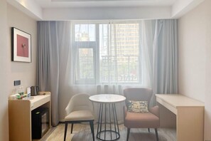 A compact room with a desk, two chairs, a small round table, and a window with curtains. - XIANG GE LI TING HOTEL (Xiuwu)