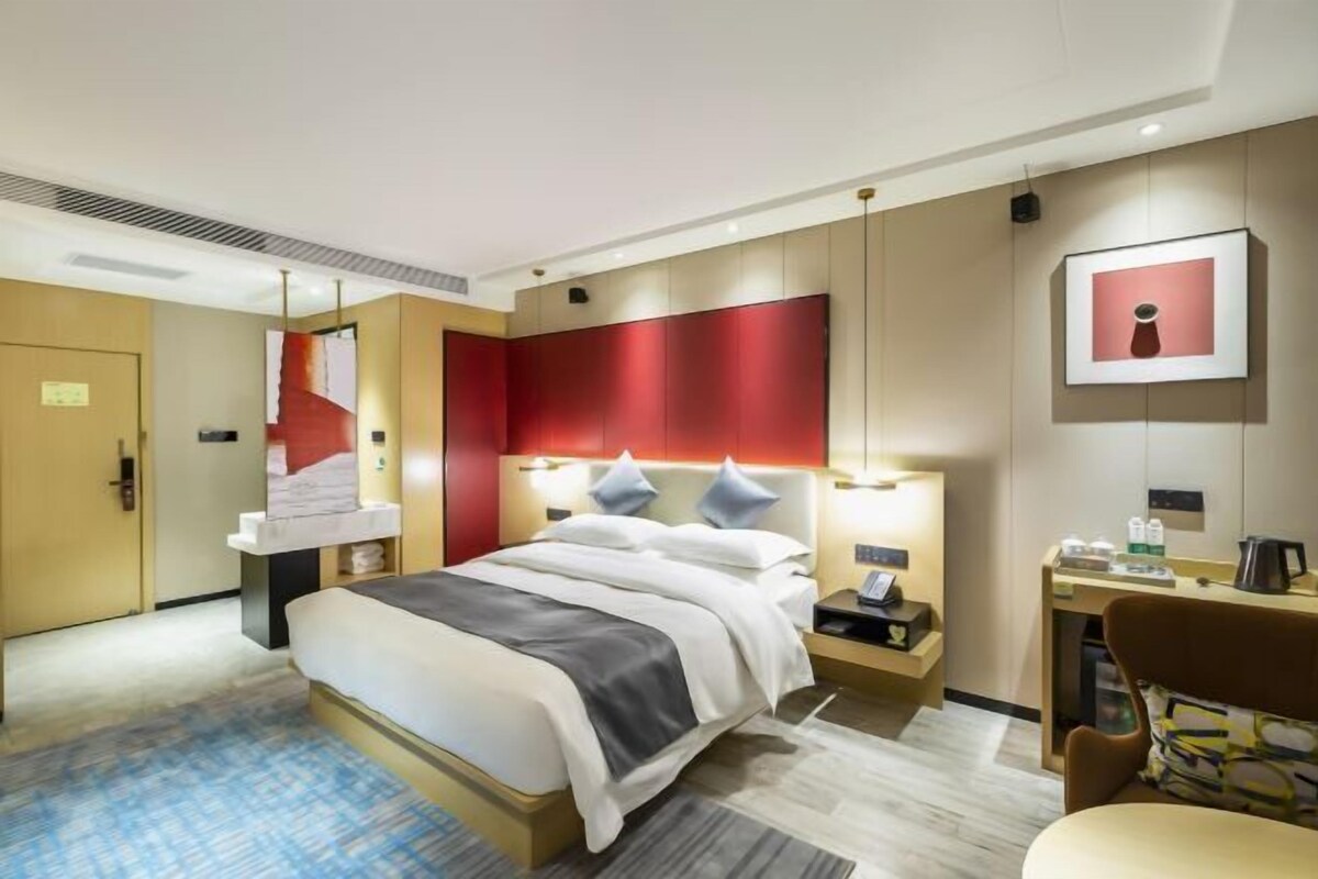 A hotel room with a bed, bedside table, lamp, and a desk with a chair.