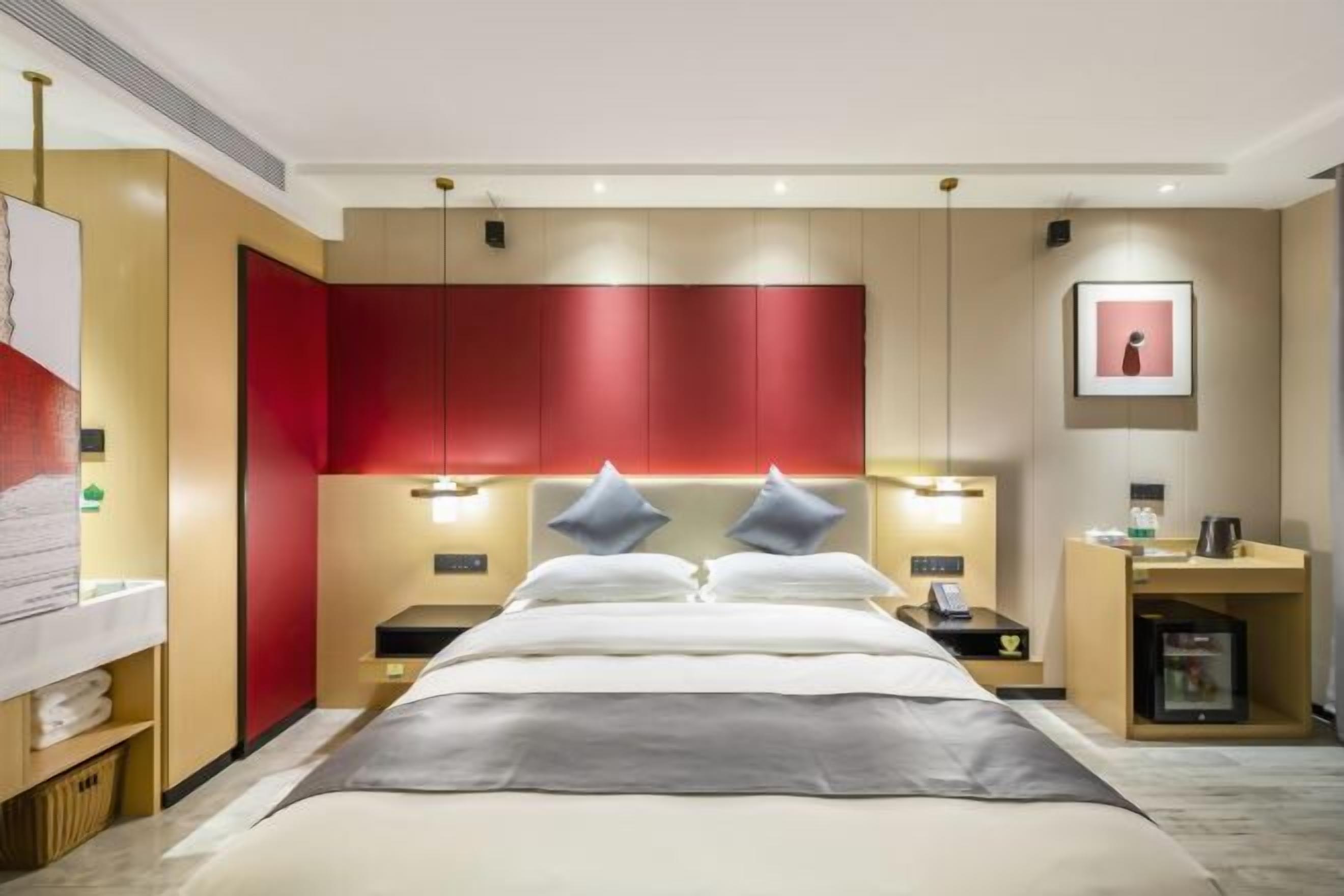 Una habitación de hotel moderna con una cama grande, mesitas de noche, una pared de acento roja y un cuadro enmarcado en la pared.