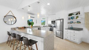 Une cuisine moderne avec des meubles blancs, un îlot central doté de tabourets de bar, des appareils en acier inoxydable, un éclairage suspendu et un grand miroir.