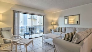 Una sala de estar moderna con un sofá, un sillón y una mesita. Se aprecia un balcón con vistas a edificios.