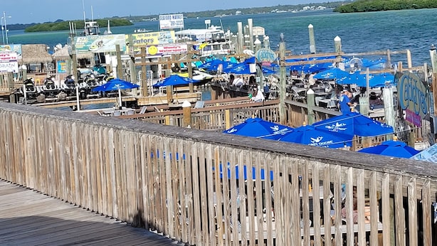 Un muelle de madera con sombrillas azules y un letrero de mercado de mariscos.