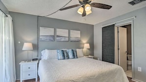 Un dormitorio con una cama, dos mesitas de noche, un ventilador de techo y tres cuadros colgados en la pared.