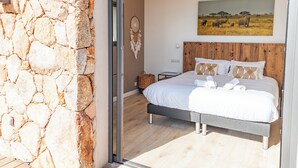Un dormitorio con pared de piedra, cama con ropa de cama blanca, cabecero de madera y un cuadro con elefantes en la pared.
