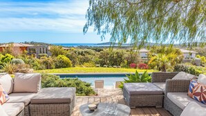 Un patio con mobiliario de mimbre, una piscina y vistas al océano y las colinas.