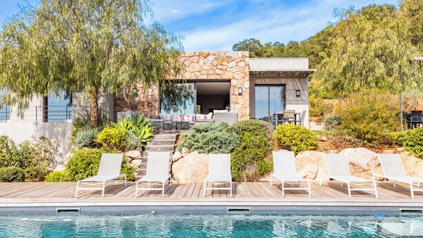 Una casa moderna con fachada de piedra, piscina y mobiliario de exterior.