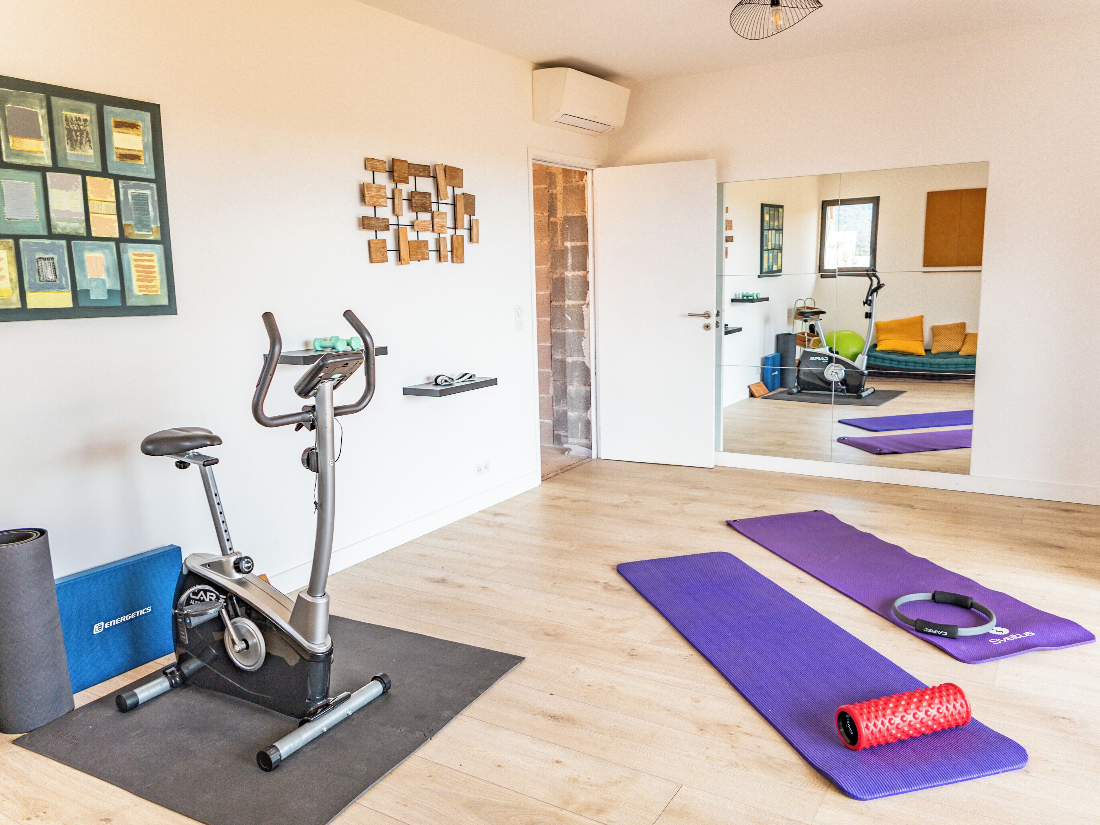 A home gym with an exercise bike, yoga mats, and a red foam roller.