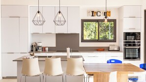 Una cocina moderna con armarios blancos, una mesa de comedor de madera y un amplio ventanal con vistas a la vegetación.