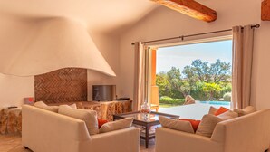 A spacious living area with two sofas, a coffee table, and a TV on a stone wall. - Villa Domaine de Pinarello (Pinarello)