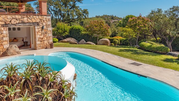 A pool with a stone structure and a view of a lush garden. - Villa Domaine de Pinarello (Pinarello)