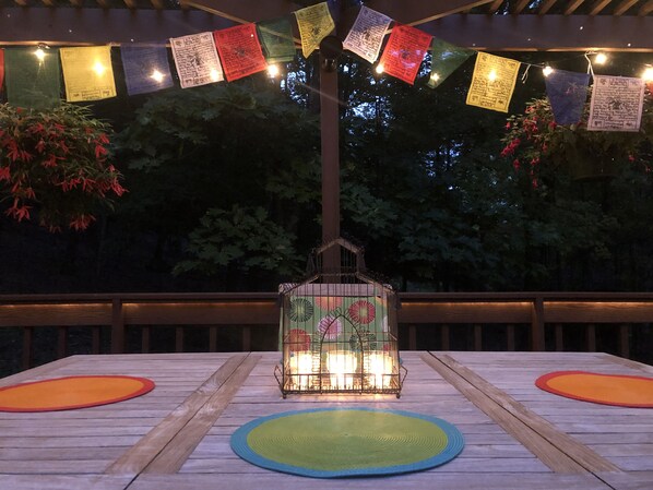 An outdoor dining area with a wooden table and chairs, a lantern, and colorful flags.