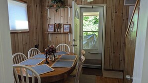 A wooden dining room with a round table, white chairs, and a door leading outside.