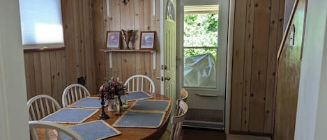 Comedor de madera con una mesa redonda, sillas blancas y una puerta que da al exterior.