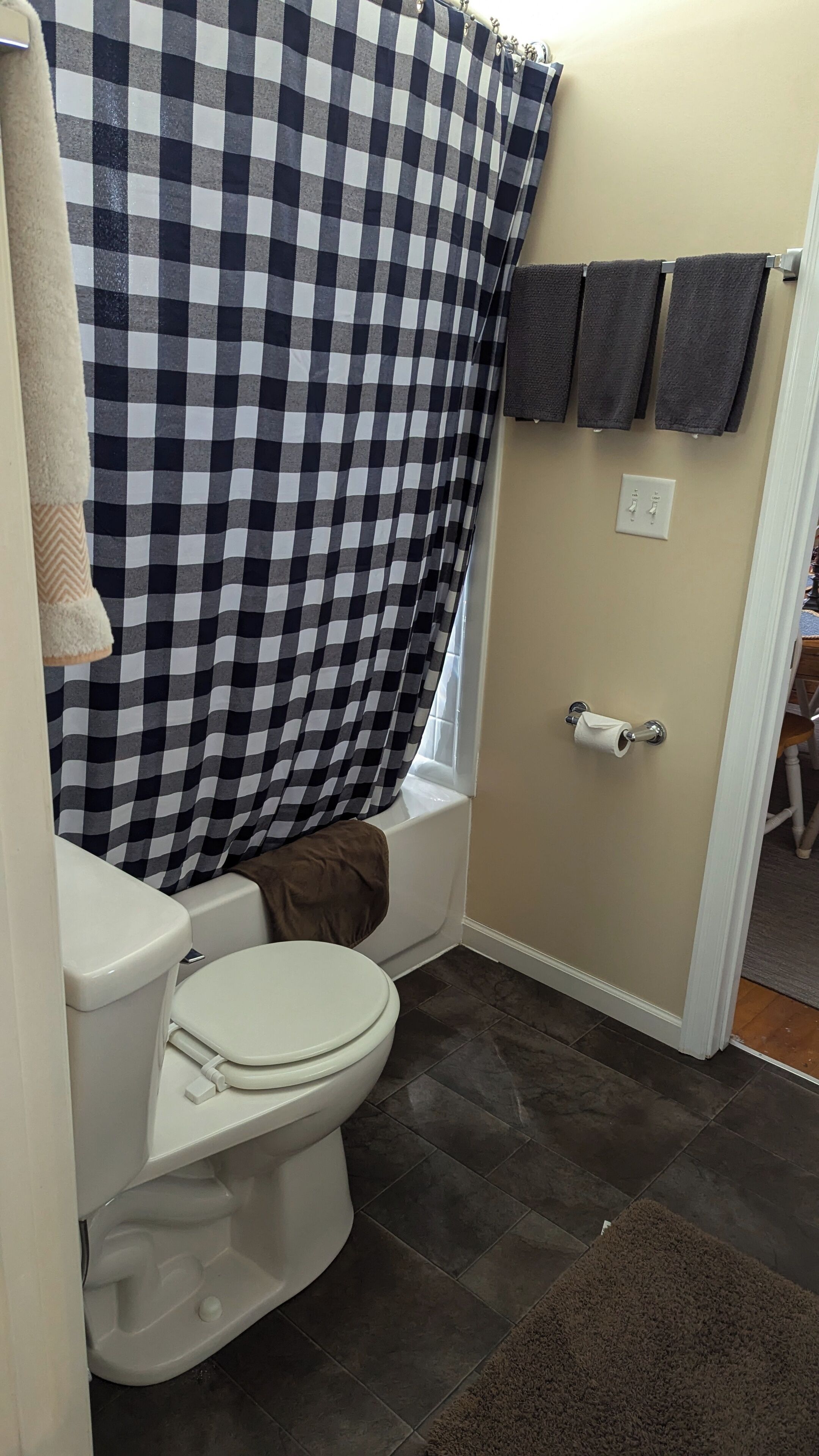 Une salle de bain avec un rideau de douche à carreaux, des toilettes, une baignoire et un porte-serviettes avec des serviettes.