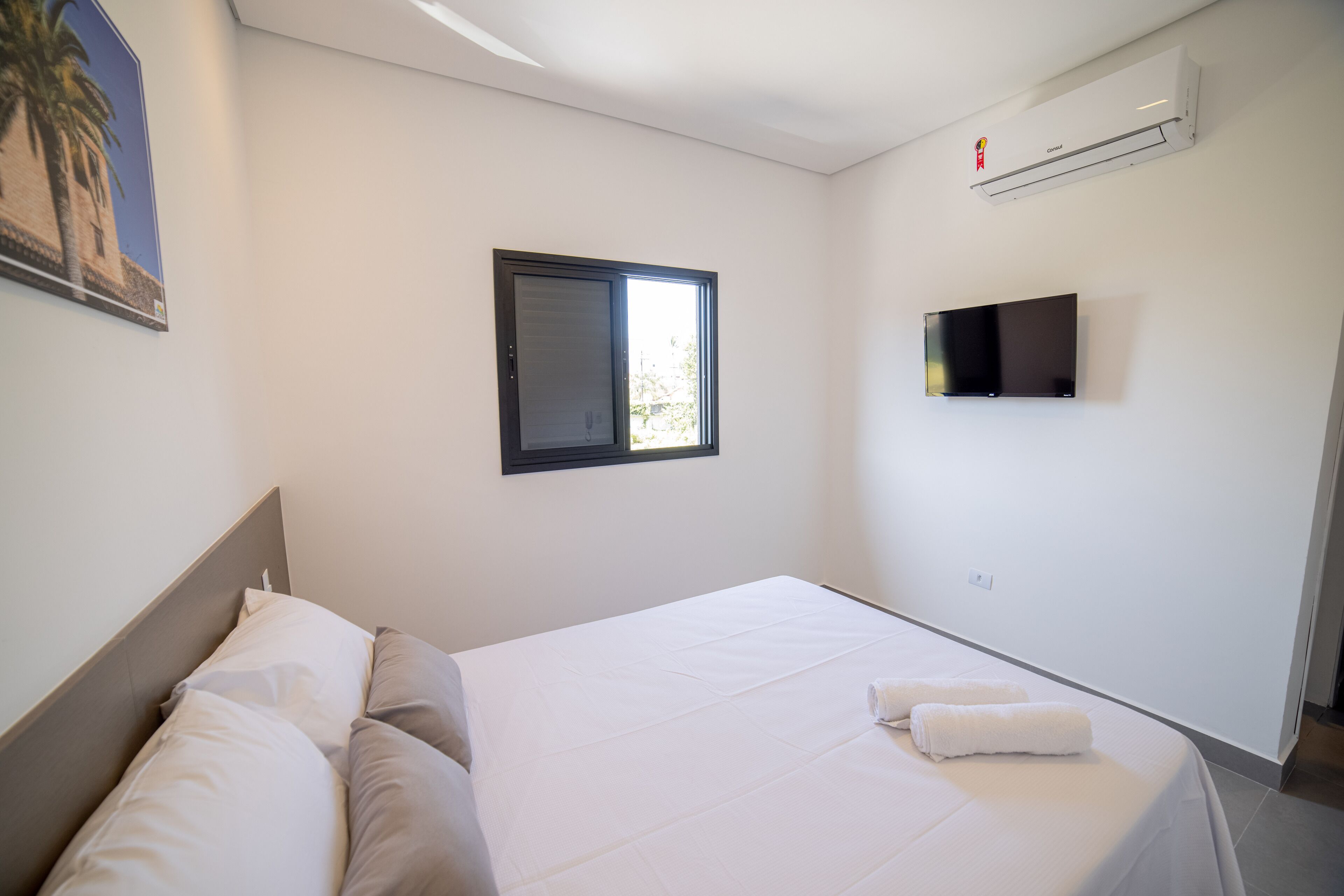 A hotel room with a bed, a window, an air conditioner, and a television.