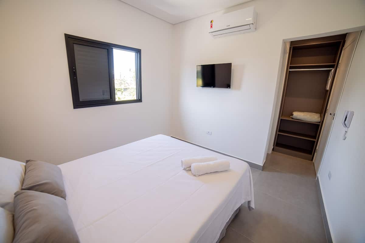 A bedroom with a bed, a TV, an air conditioning unit, and a closet.