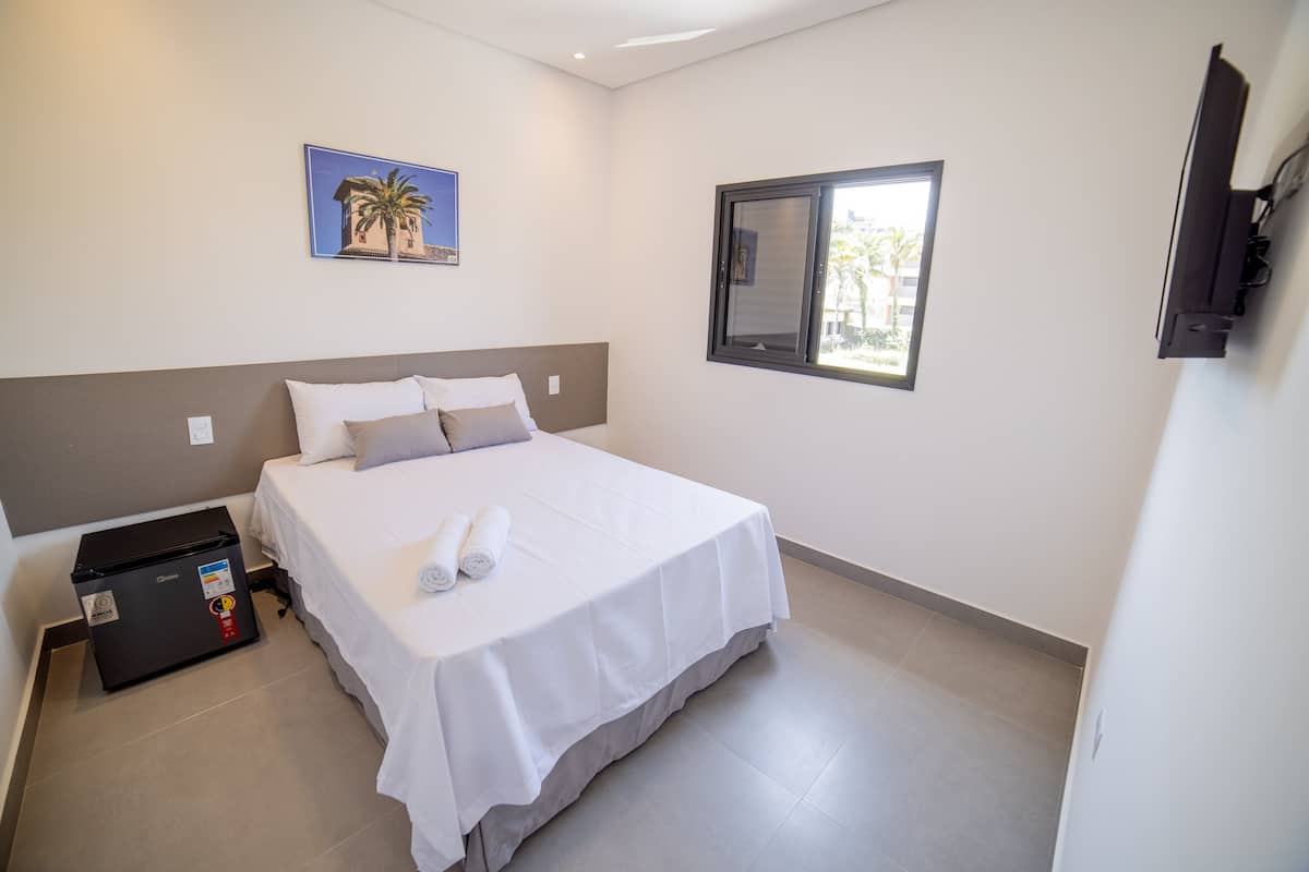 A hotel room with a bed, a small black refrigerator, a window with a view, and a wall-mounted TV.