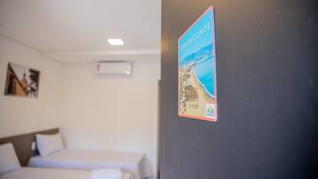 A hotel room with a bed, a wall-mounted air conditioner, and a poster of a beach scene.