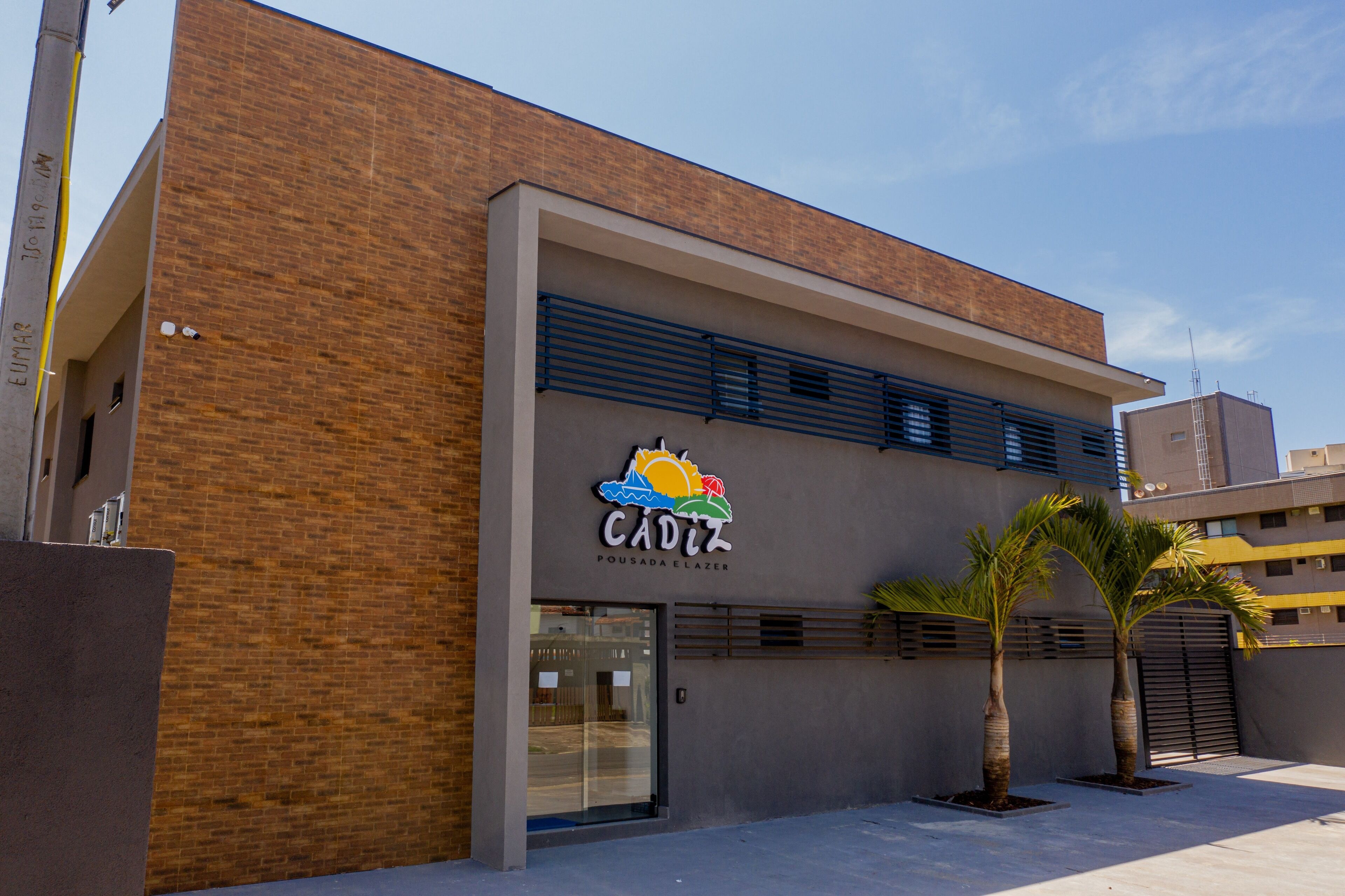 A building with a sign reading "CADIZ POUSA DA ELAZER" and two palm trees in front.
