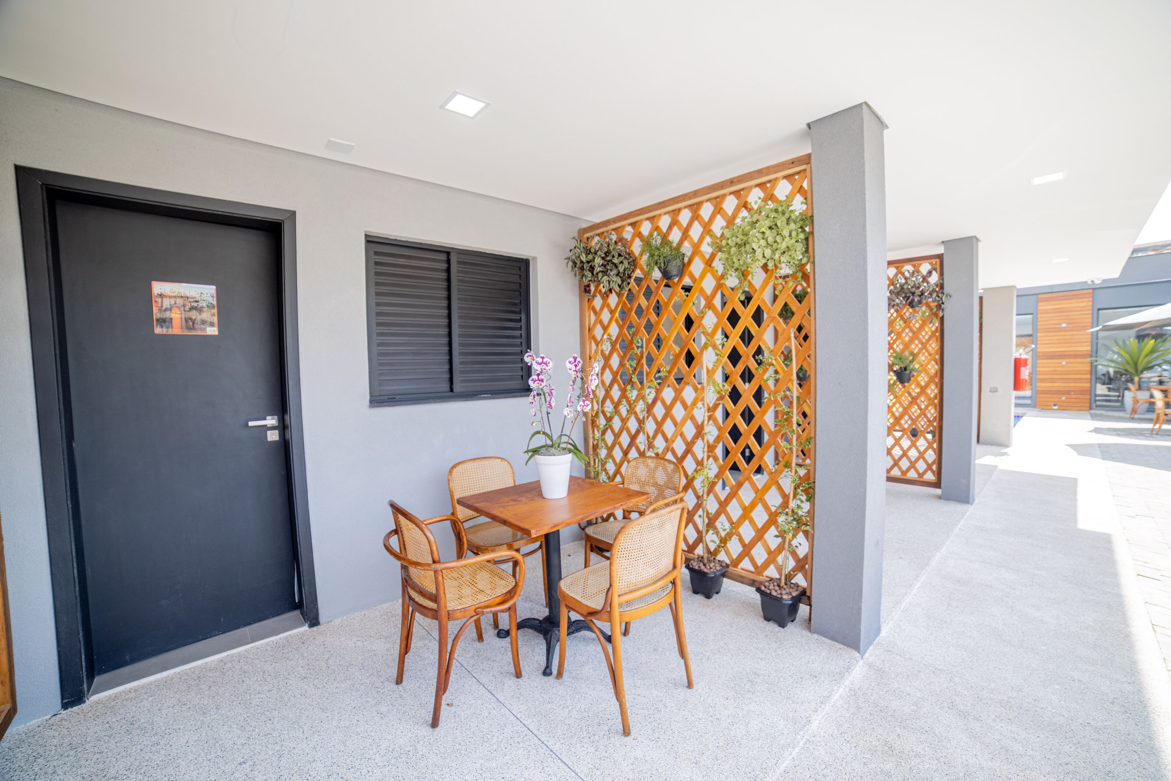 A modern outdoor seating area with a wooden table and wicker chairs, a black door, and a decorative lattice wall with plants.