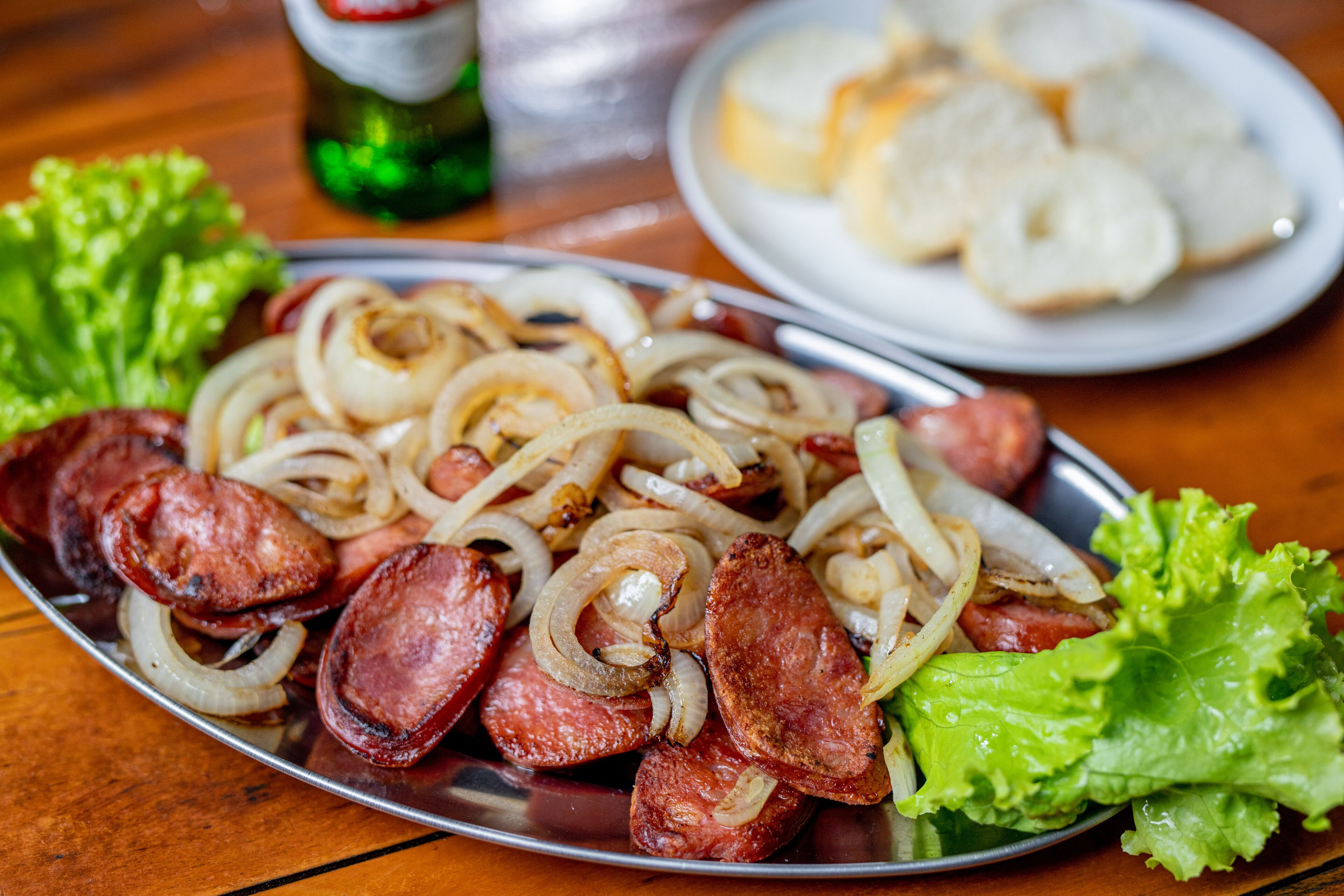 A plate of sliced sausages and onions with lettuce on a wooden table.