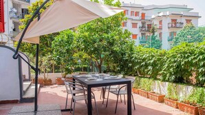 Un patio al aire libre con una mesa lista para comer, rodeada de sillas y una gran sombrilla que da sombra.