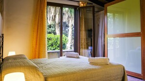 A hotel room with a bed, a window with curtains, and a view of greenery outside. - Villa Virna with garden and pool - My Rental Homes (Cinisi)