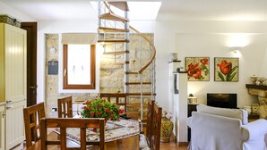 A dining area with a wooden table and chairs, a spiral staircase, and a living room with a sofa and a TV. - Villa Virna with garden and pool - My Rental Homes (Cinisi)