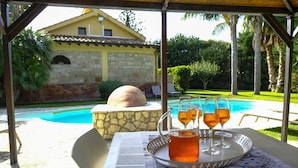 A poolside table with a tray of drinks and glasses, a stone oven, and a pool in the background. - Villa Virna with garden and pool - My Rental Homes (Cinisi)