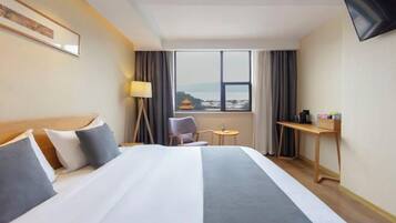 A hotel room with a large bed, a desk, a chair, a TV, and a window with a view.