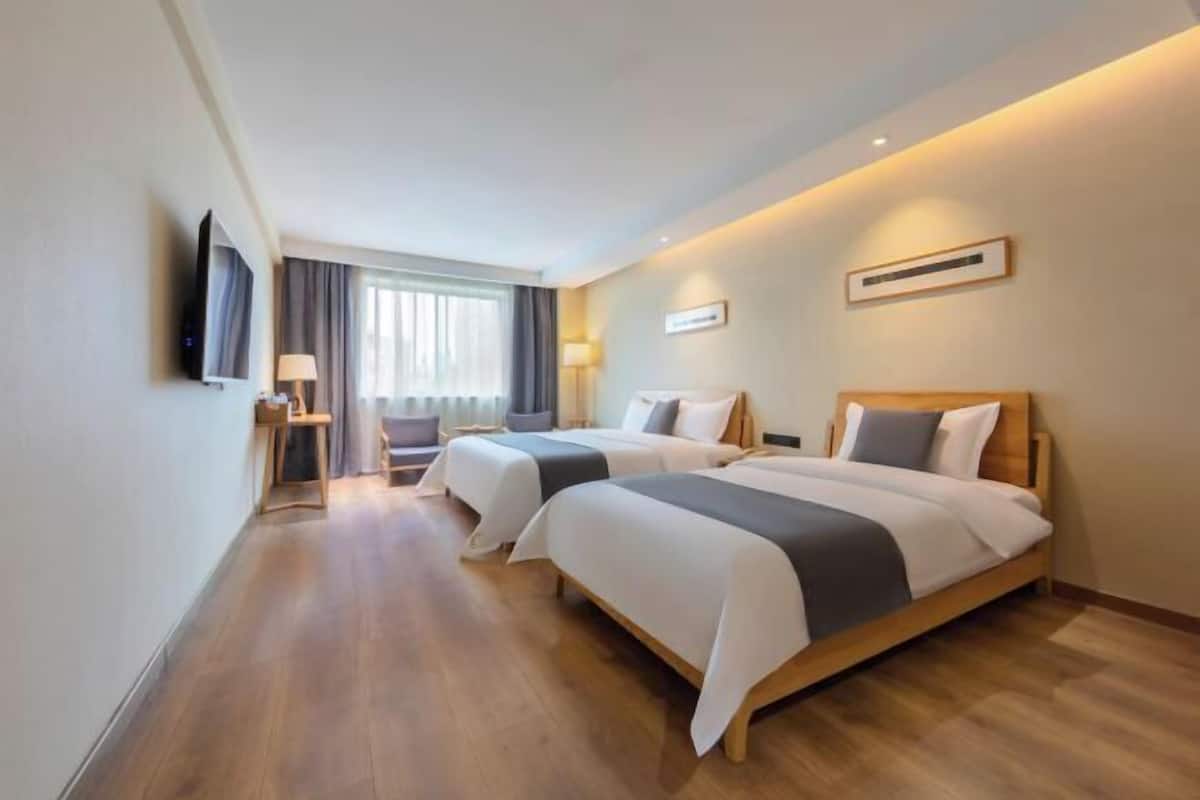 A hotel room with two beds, a TV, a desk, and a window with curtains.