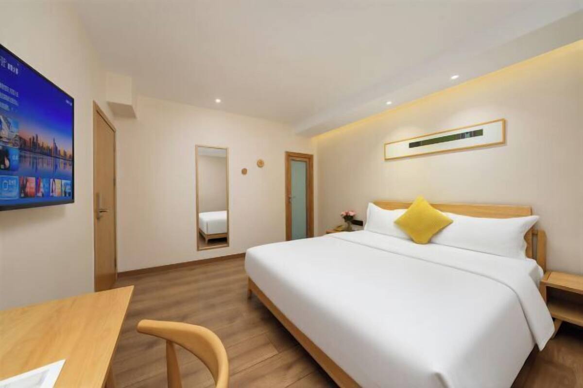 A hotel room with a bed, a desk, a chair, a mirror, and a television on the wall.